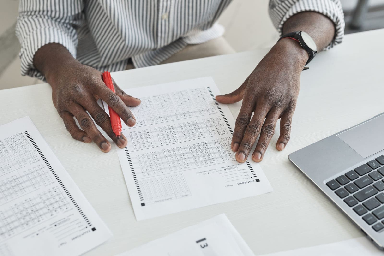 An educator marking exam papers with a red pen at a desk