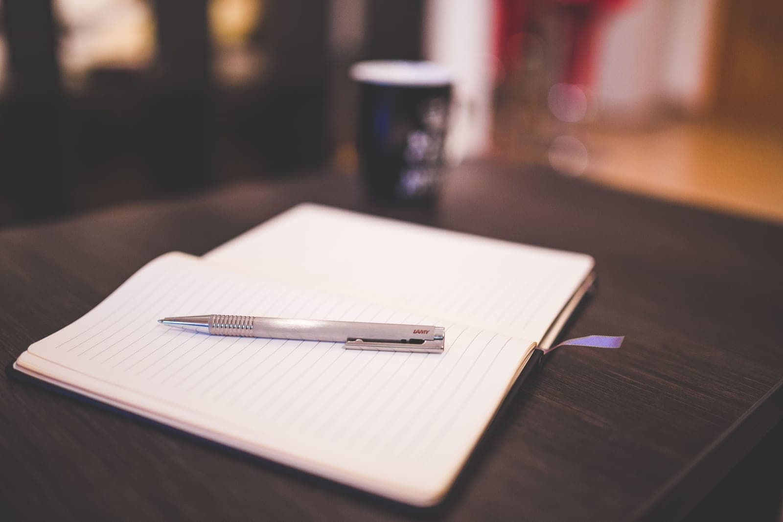 An open lined notebook with a silver pen lying on a dark wooden table