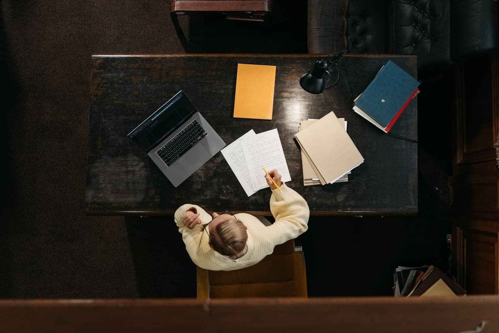 A person working at a wooden desk with documents, folders and a laptop