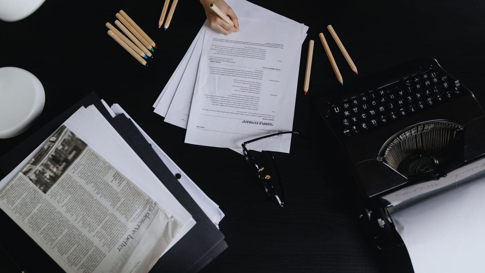 Overhead view of a desk with printed pages, a typewriter and coloured pencils