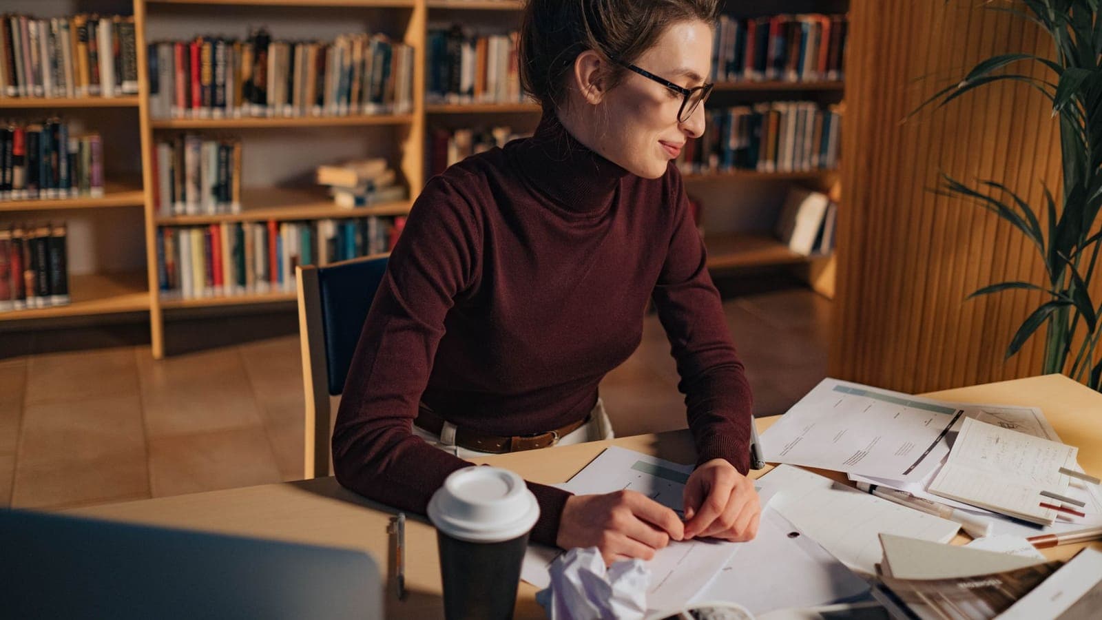 Researcher in a library studying printed papers with glasses on