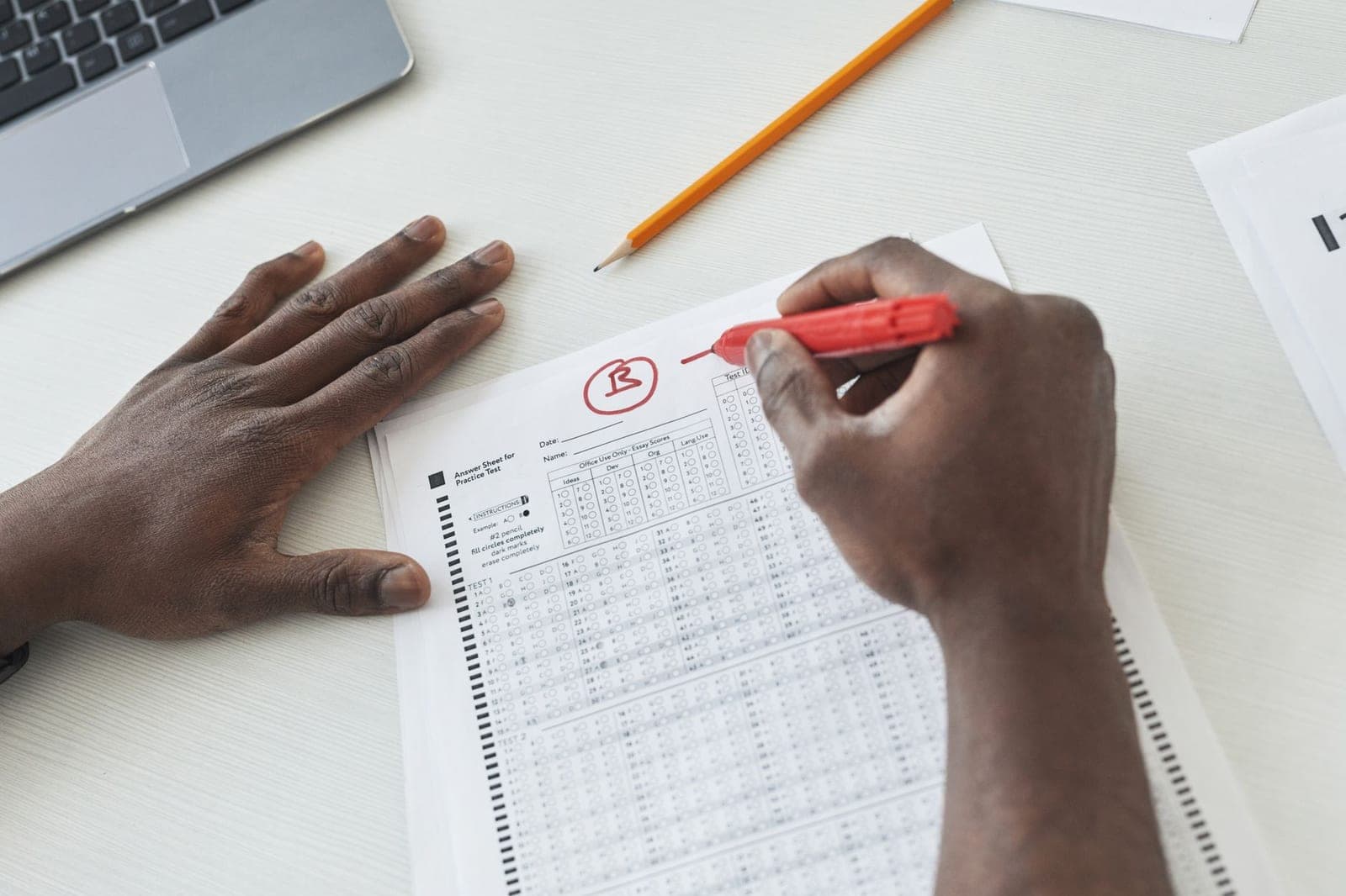 A teacher marking multiple choice exam papers with a red pen on a desk