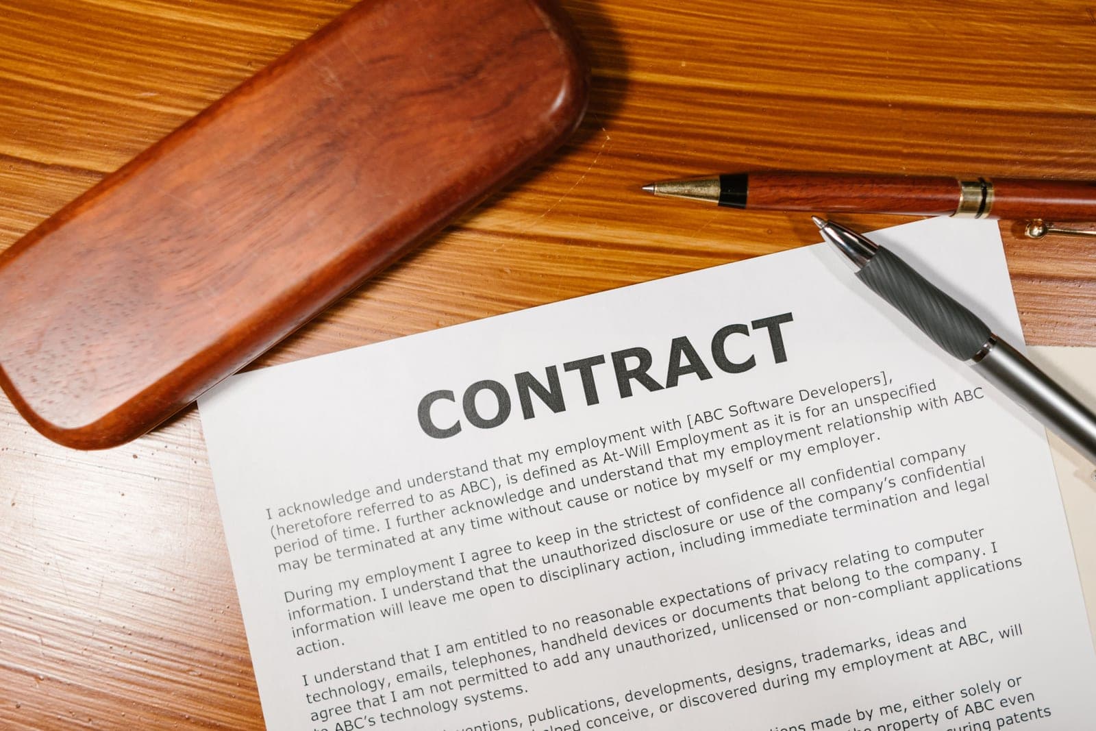 A printed contract and a pen lying on a wooden desk, photographed from above